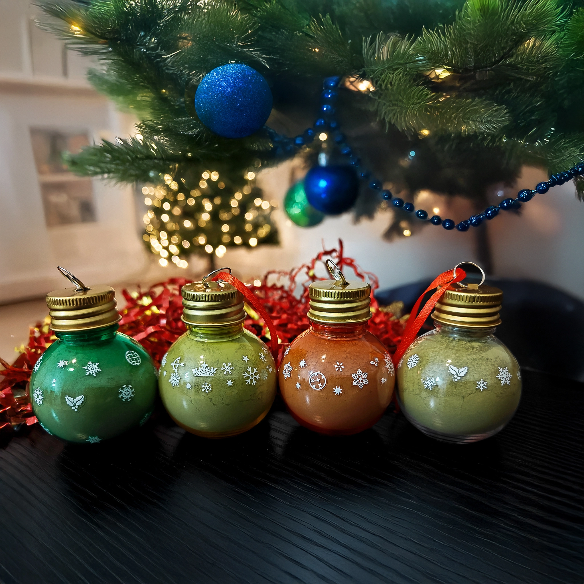 Christmas-Gift-Set-Pic1 holiday product photo of a white gift box open with tinsel and scattered confetti. inside are four christmas ornaments filled with kratom powder.